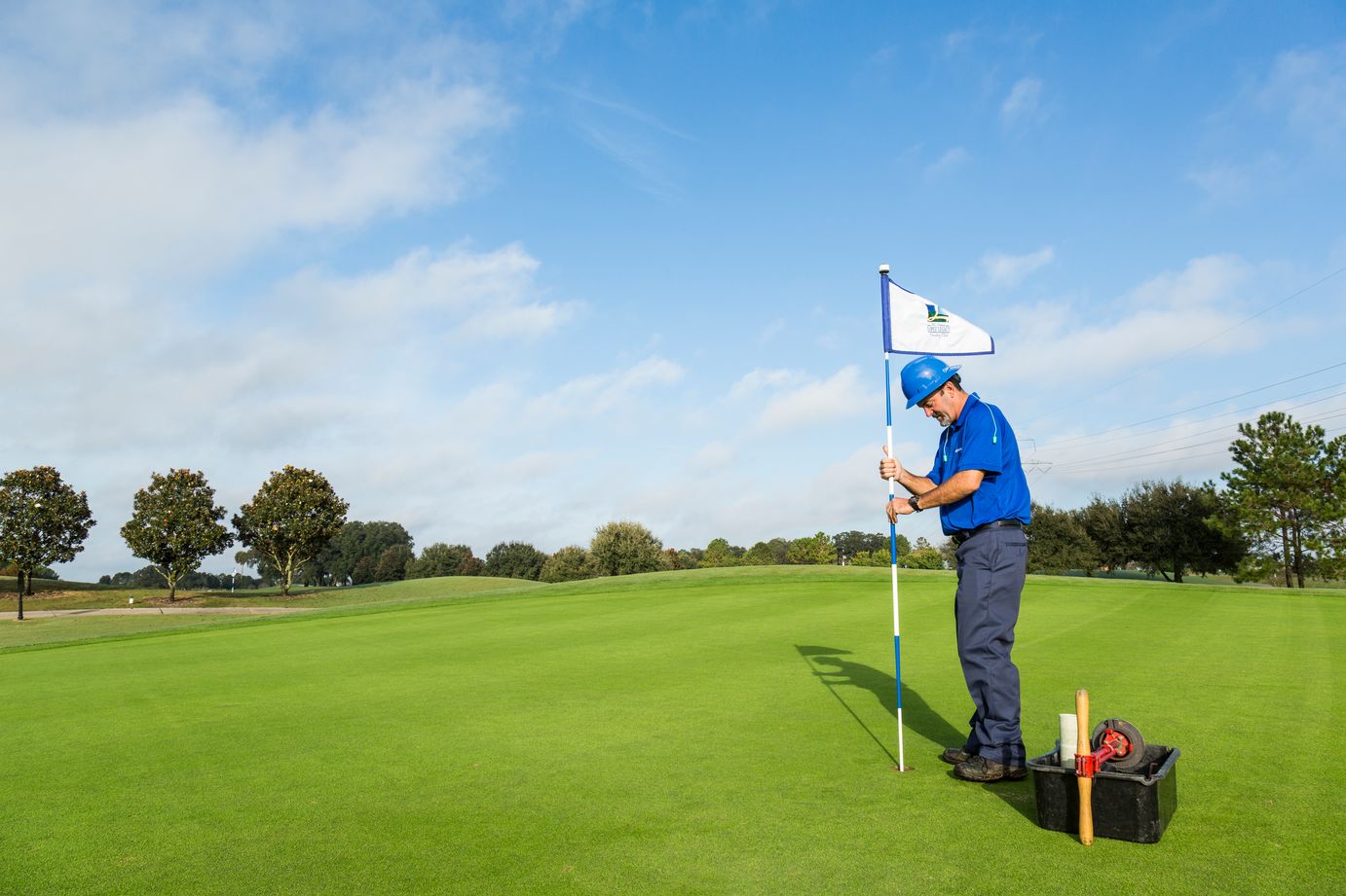 golf course maintenance crew member placing a flag on a hole